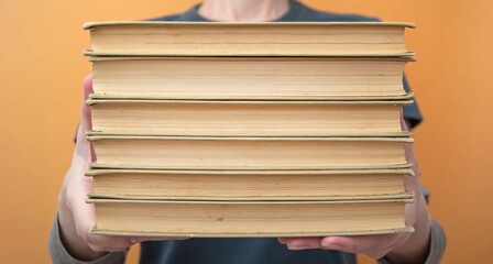 A woman holds a stack of old paper books at arm's length. Educational concept. Selective focus.