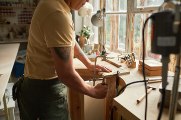 Side view of tattooed artist cutting wood while creating handmade pieces in workshop