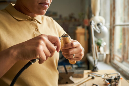 Close up of female artist creating handmade jewelry with wooden tools in cozy workshop lit by sunlight, copy space