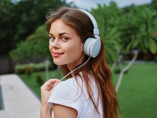 Woman portrait in headphones happiness smile in a white T-shirt listening to music and walking down the street, in front of palm trees