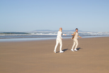 Gay man running and reaching hand to boyfriend. Middle aged homosexual couple spending time on beach. LGBT concept