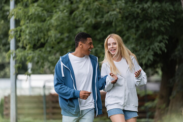 Obraz premium excited blonde woman gesturing while talking to african american boyfriend in park