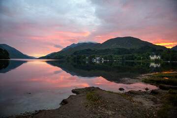 Colourful sunset in the Scottish Highlands with mountains, houses, sky and light reflected off the lake