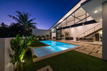 Tropical villa view with garden, swimming pool and open living room at sunset - obrazy, fototapety, plakaty
