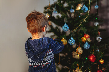 Little cute caucasian boy decorating Christmas tree with twinkling decorations.