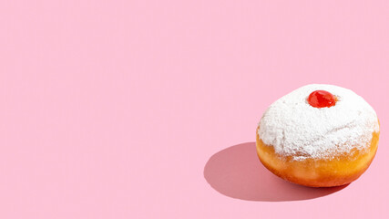 Hanukkah jelly doughnut Sufganiyah on pink background with copy space.