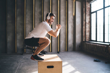 Smiling man doing jump exercise on plyometric box in gym
