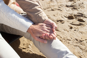 Gays sitting on sand and holding hands. Close-up of unrecognizable men spending time on beach. Closeness concept