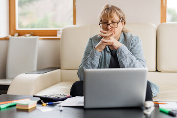 Active mature woman using a laptop for remote work from the home office. Video conference, video meeting. Senior teacher leads webinar	
