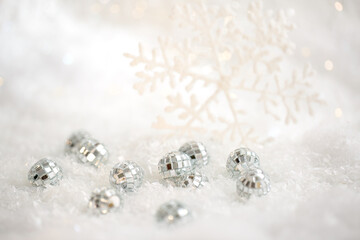 Christmas snowflake and small mirror balls on a white snow. Blurred background with beautiful bokeh. Shallow depth of field. Copy space. Airy atmosphere. Soft focus. 