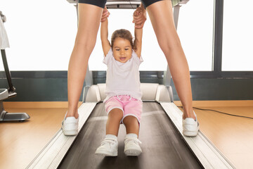 Crop mother playing with daughter on treadmill 