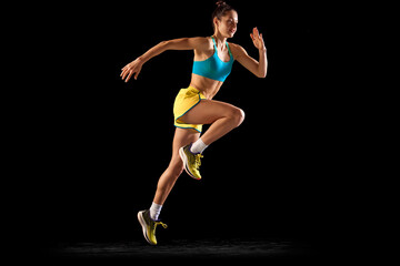 Young sportive woman, runner and jogger in motion action isolated on black background. Sport, fitness, energy, movements concept