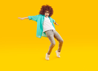 Fototapeta na wymiar Happy kid dancing and having fun. Funny cheerful excited child boy in casual clothes and curly wig dancing on an amber orange yellow color studio background