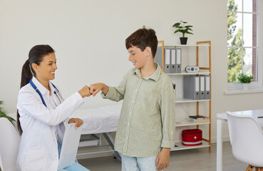 Obraz premium Happy doctor and a child patient greeting each other with a fist bump. Friendly pediatrician and a little school boy meet, smile and give each other a fist bump