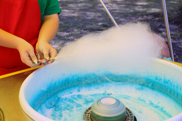 A portion of cotton candy. Hands hold a stick for making dessert. Rest with family in the amusement park.