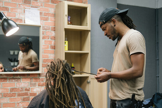 African master hairdresser making dreadlocks for young woman in hair salon