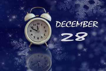 Calendar for December 28: white alarm clock on a blue background with bokeh, reflection from objects, name of the month december, numbers 28