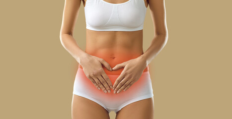 Girl suffering from severe period cramps. Woman in underwear having acute menstrual pain standing on beige background holding hands on red inflamed stomach, cropped shot, banner. Menstruation concept