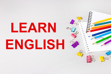 Notebooks, colored pencils and paper clips on a light gray table. The inscription LEARN ENGLISH. Banner