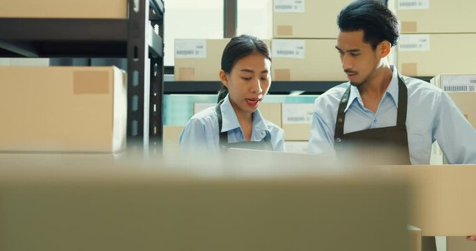 Asian business partner girl hold laptop and man wear formal shirt hold cardboard box training inventory online stock data program for delivery customer at warehouse. Startup small business concept.