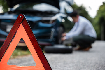 Asian businessman car broken has problems with wheel of his car during go to work in morning he changing replace rubber tire on wheels, business man have warning sign on road, problem transportation