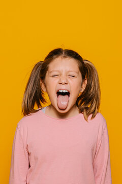 Funny little girl sticking out tongue on yellow background
