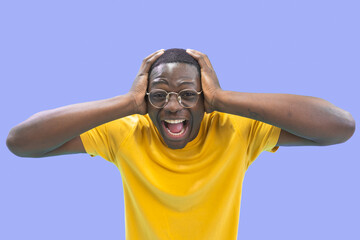 Handsome African American man crazy, excited and scared with hands on head, afraid and surprised of shock with open mouth wearing yellow shirt and glasses over purple background. High quality photo