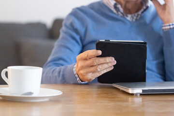 Fototapeta na wymiar Mature man using tablet while working in home office. Close-up shot of unrecognizable elderly businessman looking at tablet screen, solving business problems. Digital device, workplace concept