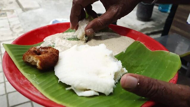 Close up of man eating idly and vada placed over the banyan leaf in plate
