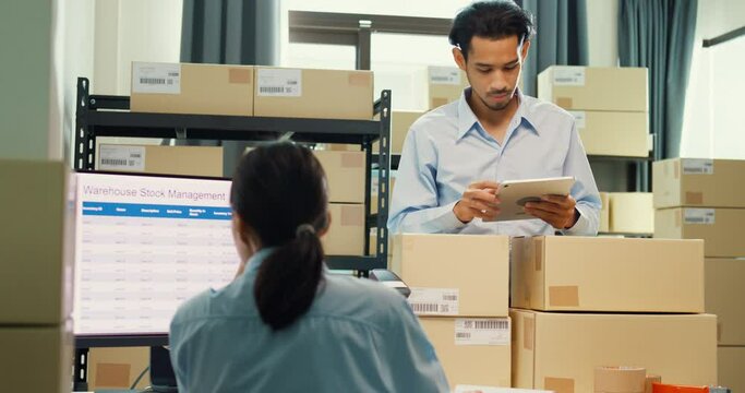 Asian business partner man hold tablet and girl partner wear formal shirt sit front desk computer meeting discuss inventory stock online data in delivery at warehouse. Startup small business concept.