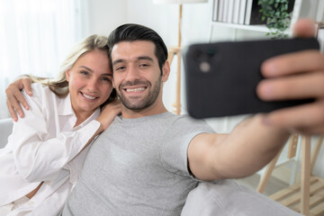 Caucasian couple sitting on the couch and looking at the smartphone screen.