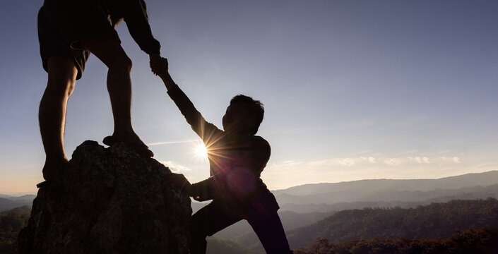 Silhouette of helping hand between two climber. couple hiking help each other silhouette in mountains with sunlight. The men helping pull people up from high cliffs