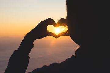 Silhouette. Woman forming a heart shape during sunrise. God is love concept. Heart shape. Mountain tourism. showing love Love and feelings, dedication and hope.