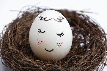 Close up of a beautiful white egg in a wicker nest on a white background. Cute face with red freckles. The view is straight. Spring postcard. Happy Easter.