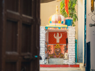 An open door with a small sunlit Hindu temple to venerate the goddess Kali decorated with a crown and necklaces and some tigers. Udaipur, Rajasthan, India