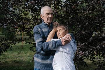 Fototapeta premium Elderly couple husband and wife standing outdoor in summer park, hugging relaxing enjoying sunny day and love