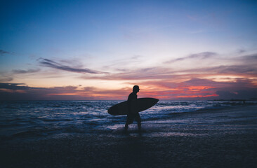 Silhouette of anonymous surfer with surfboard on sand beach