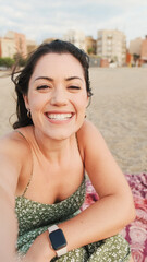 Fototapeta na wymiar Young woman sitting on sandy beach and using mobile phone, making video cal