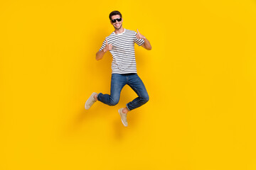 Full length photo of confident pretty man wear white t-shirt dark glasses showing thumbs up jumping high isolated yellow color background