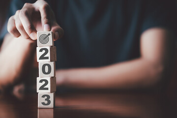 2023 New Years Businessman holding wooden cube with target board icon and 2023 on wooden table. Goals and planning for success in marketing business, achieve the objective concept. Free copy space