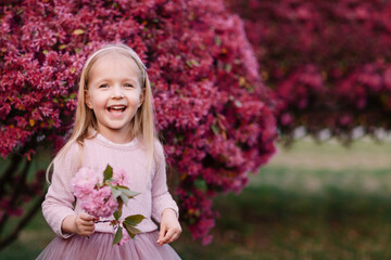 Happy little caucasian girl holding hand blooming branch of sakura. Background Color of the year 2023 viva magenta. Trendy colors concept