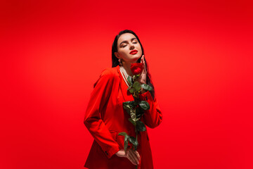 Pretty brunette woman in jacket holding rose isolated on red