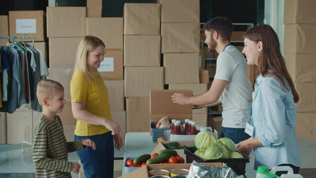 Friendly Volunteer Giving Donation Box With Food to Woman and Her Son at Distribution or Refugee Assistance Center. The Concept of Social Aid. Internally Displaced Persons