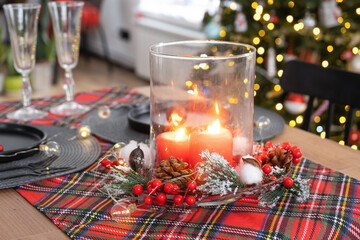 Festive table set in the living room for Christmas and New year in loft style. Christmas tree, black plates and forks, woven napkins, trendy tableware, cozy interior of the house