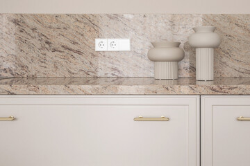 Beige granite kitchen counter with electric outlets on stone wall, two elegant beige vases. Modern kitchen concept.