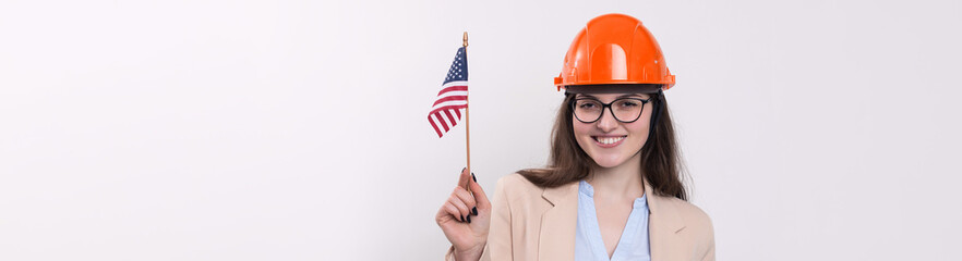 A girl in a construction helmet and an American flag stands happy on a white background.