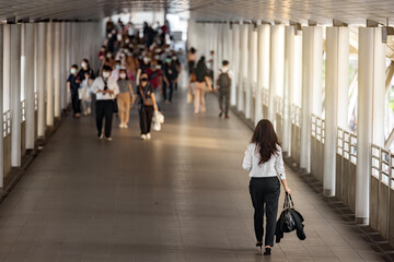 Obraz premium Back side view of Asian businesswoman going to work standing out from the crowd at the busy city street and blurred background Crowd of people walking street wearing masks in rush hour working day. 