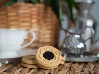 An artistic still life with pink peonies in a wicker basket, a cup of coffee, cream and cookies. Horizontal photo.