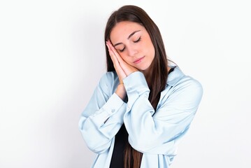 Young caucasian woman wearing blue overshirt over white background sleeping tired dreaming and posing with hands together while smiling with closed eyes.