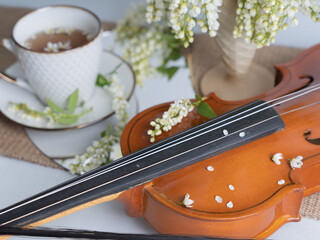 Artistic still life with a bouquet of bird cherries, a cup of tea and a violin. Horizontal photo.